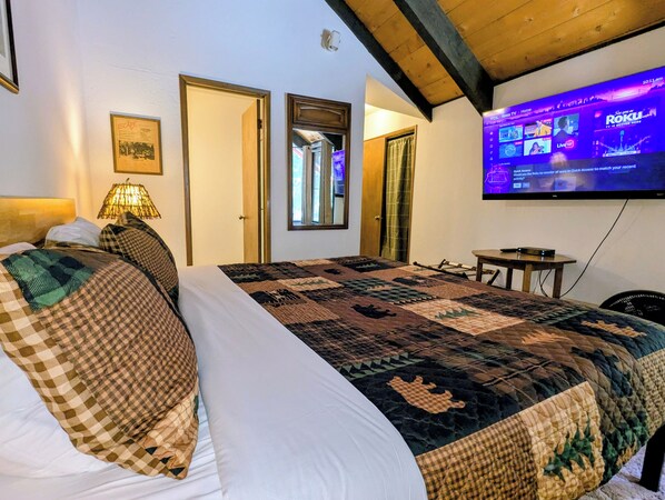 A hotel room with a large bed, a television mounted on the wall, and a wooden ceiling.
