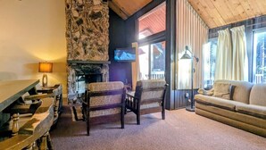 Una sala de estar acogedora con chimenea de piedra, vigas de madera, un sofá y una televisión.