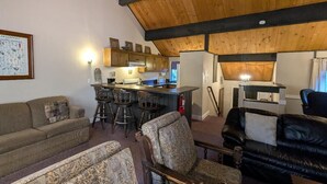 Una sala de estar acogedora con techos altos, una zona de comedor con taburetes de bar y una cocina con armarios de madera.