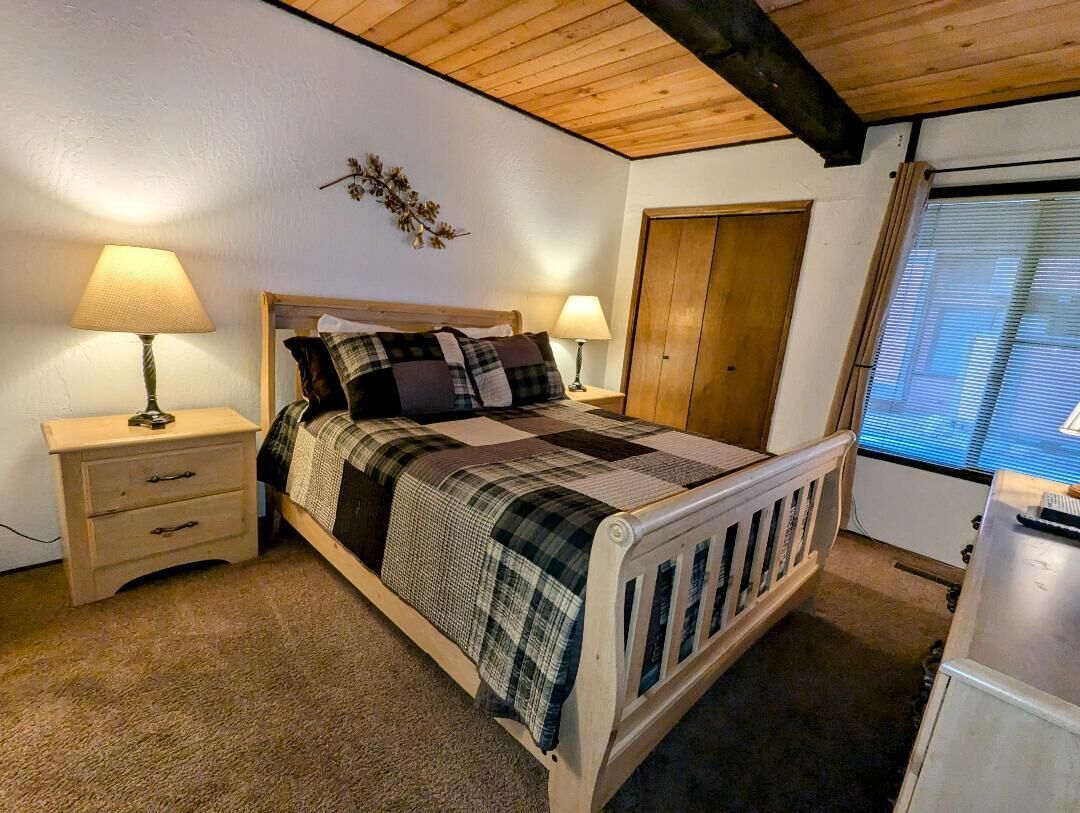 A bedroom with a wooden bed, two bedside tables with lamps, a wardrobe, and a window with blinds.