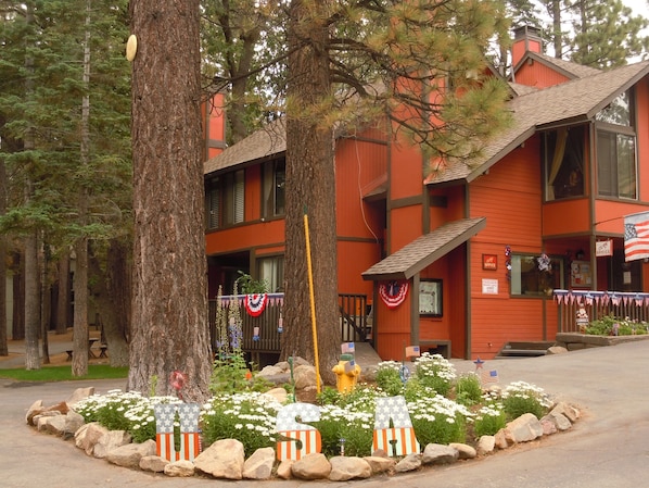 Un bâtiment rouge, orné d’un drapeau, avec une borne d’incendie et un jardin agrémenté de rochers et de fleurs.