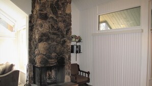 A living room with a stone fireplace, a wooden chair, a sofa, and a window with blinds.