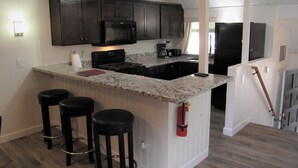 A kitchen with dark cabinets, a granite countertop, and a built-in microwave. There are two black barstools and a fire extinguisher mounted on the wall.