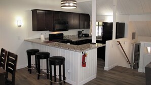 A modern kitchen with dark cabinets, a granite countertop, and a central island with bar stools.
