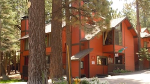 A red lodge with a stone foundation, surrounded by trees and a flower bed. - Seeking the best location? Ski, Hike, Relax, Repeat in this Cozy Townhouse (Big Bear Lake)