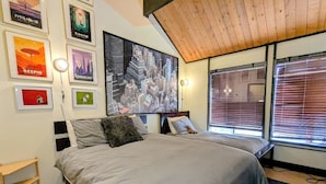 A bedroom with a bed, a nightstand, a wall-mounted shelf, and a large window with blinds. - Seeking the best location? Ski, Hike, Relax, Repeat in this Cozy Townhouse (Big Bear Lake)