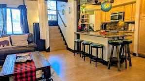 A cozy living room with a sofa, a coffee table, and a kitchen area with a bar stool and a microwave. - Seeking the best location? Ski, Hike, Relax, Repeat in this Cozy Townhouse (Big Bear Lake)