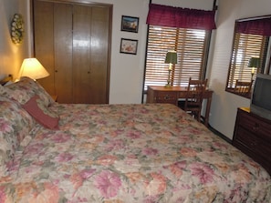 Un dormitorio con cama, escritorio, silla, televisor y armario.