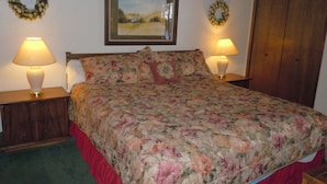 Un dormitorio con colcha estampada, dos lámparas de noche, un cuadro enmarco con paisaje y un armario de madera.