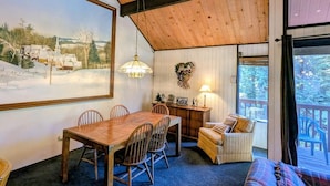 Una habitación acogedora con techo de madera, una mesa de comedor con sillas, un sofá y un ventanal que ofrece vistas a un paisaje nevado.
