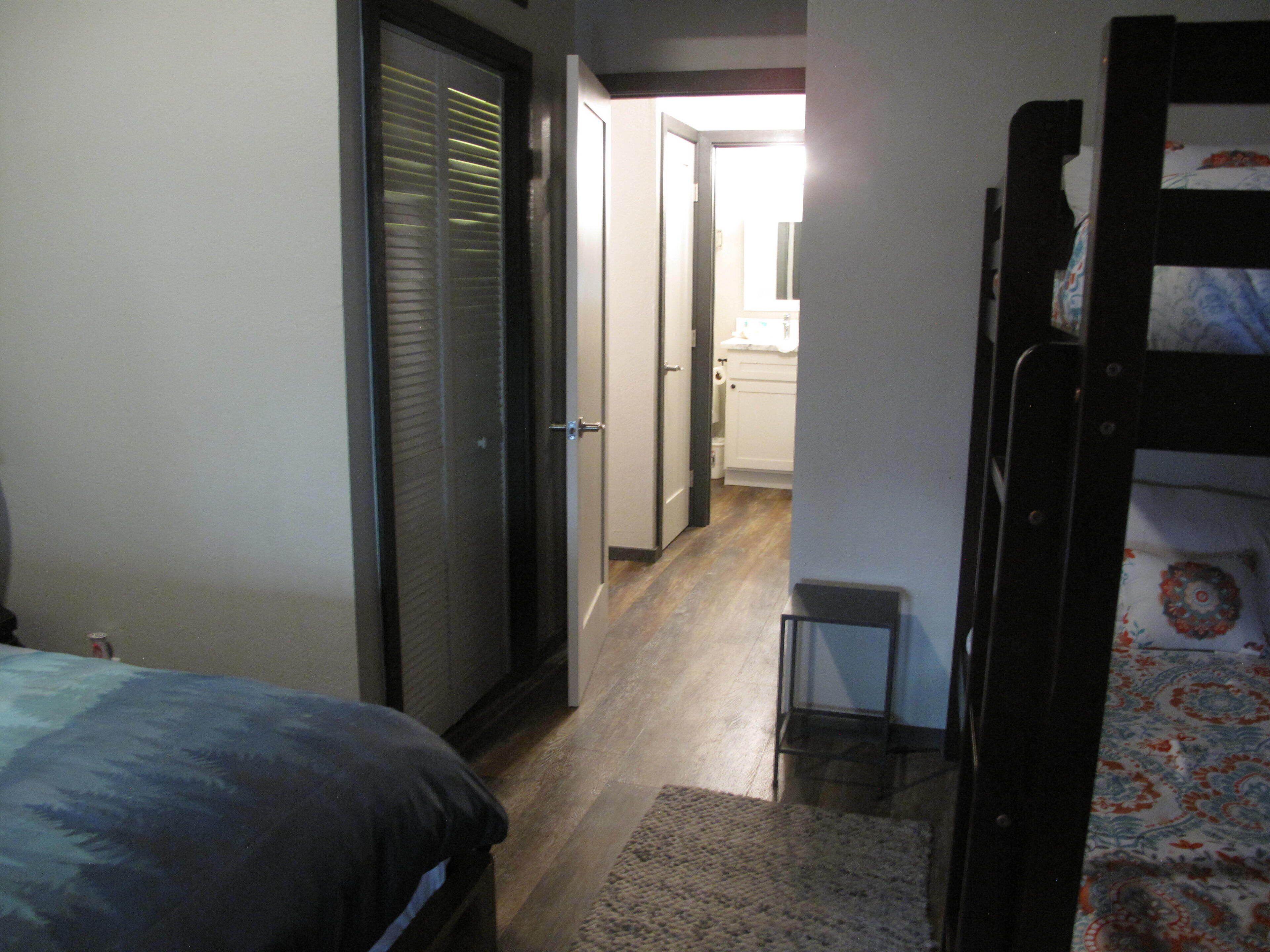 A narrow hallway with a bed on the left, a small stool, and a bunk bed on the right.
