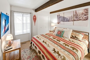 Ein Schlafzimmer mit Bett, Fenster, Tür, einer Wandlampe und einem Gemälde.