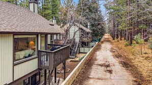 A house with a deck, a chimney, and a pathway leading through a forest.