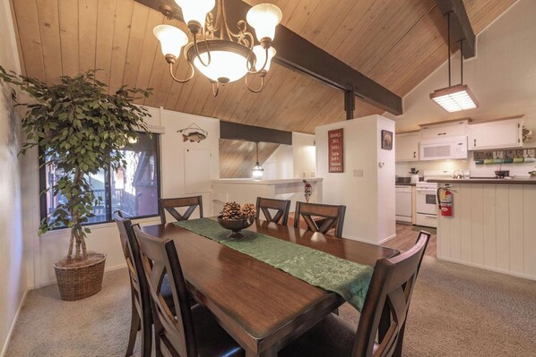 A dining area with a wooden table, chairs, a chandelier, and a potted plant.
