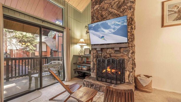 Un salón acogedor con chimenea de piedra, televisor montado encima y balcón con vistas al exterior.