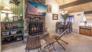 Una sala de estar acogedora con chimenea de piedra, un televisor montado encima y un comedor con muebles de madera.