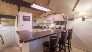 Una cocina con una isla central, taburetes de bar, un microondas y un letrero que dice "BE OUR GUEST".