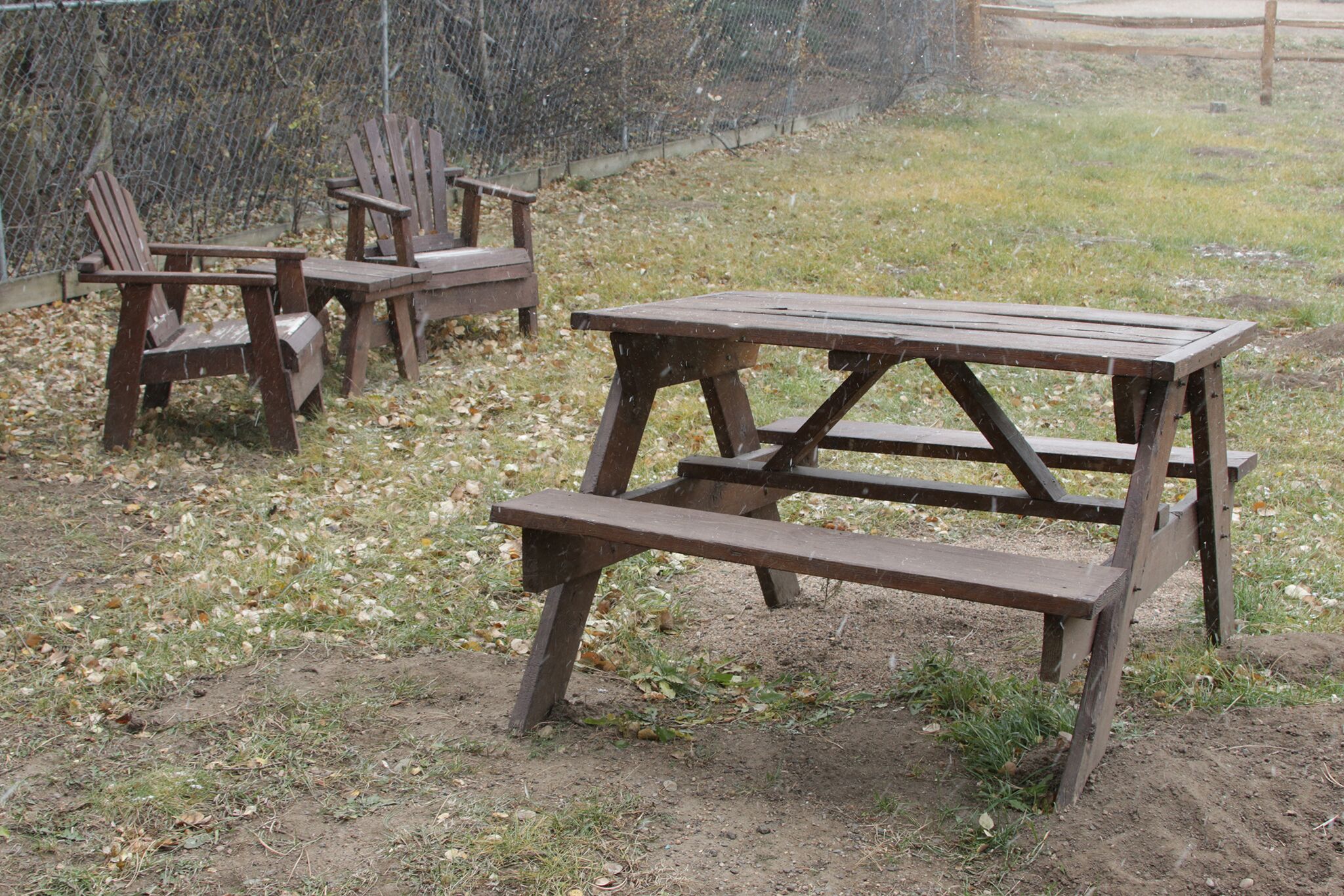 Ein Picknicktisch mit Stühlen auf einer Rasenfläche, im Hintergrund ein Zaun.