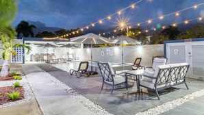Un patio al aire libre con mesas, sillas, sombrillas y luces colgantes.