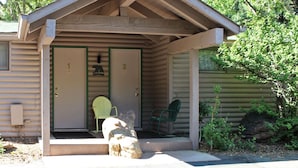 Una cabaña de troncos con un porche, dos puertas y una chimenea.