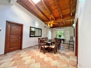 Ein Essbereich mit Holzbalkendecke, einem großen Tisch und umringenden Stühlen sowie einem Deckenventilator.