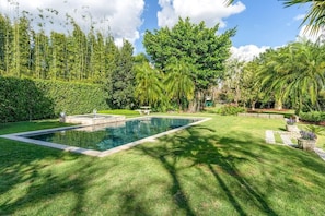 A rectangular swimming pool surrounded by well-manicured grass, with a variety of trees and shrubs in the background.