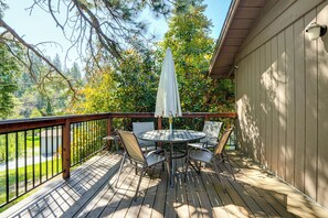Une terrasse en bois avec une table ronde et des chaises, un parasol et une rambarde.
