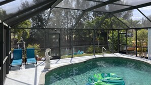 Une piscine couverte à l’eau claire, entourée d’une structure en verre, avec des chaises longues bleues et une statue décorative.