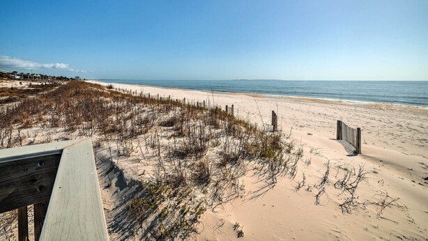 A beach with a wooden boardwalk leading to the shore, sandy dunes, and a clear blue sky. - Mexico Beach Getaway w/ Patio - Steps to Beach! (Mexico Beach)