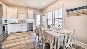 A modern kitchen with white cabinets, a dining area with a table set for four, and a large window with blinds. - Mexico Beach Getaway w/ Patio - Steps to Beach! (Mexico Beach)