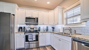 A modern kitchen with white cabinets, stainless steel appliances, a granite countertop, and a window with blinds. - Mexico Beach Getaway w/ Patio - Steps to Beach! (Mexico Beach)