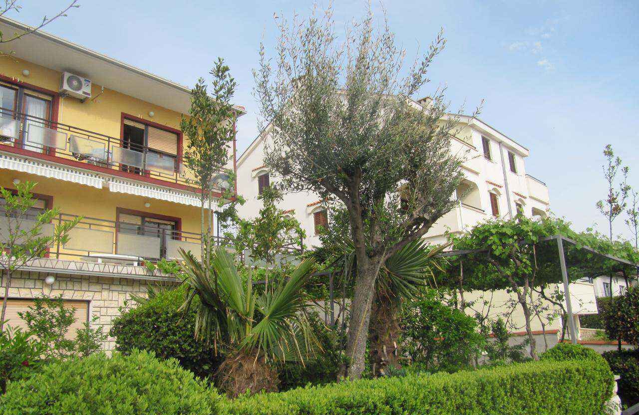 A two-story building with balconies, surrounded by lush greenery and a clear sky.