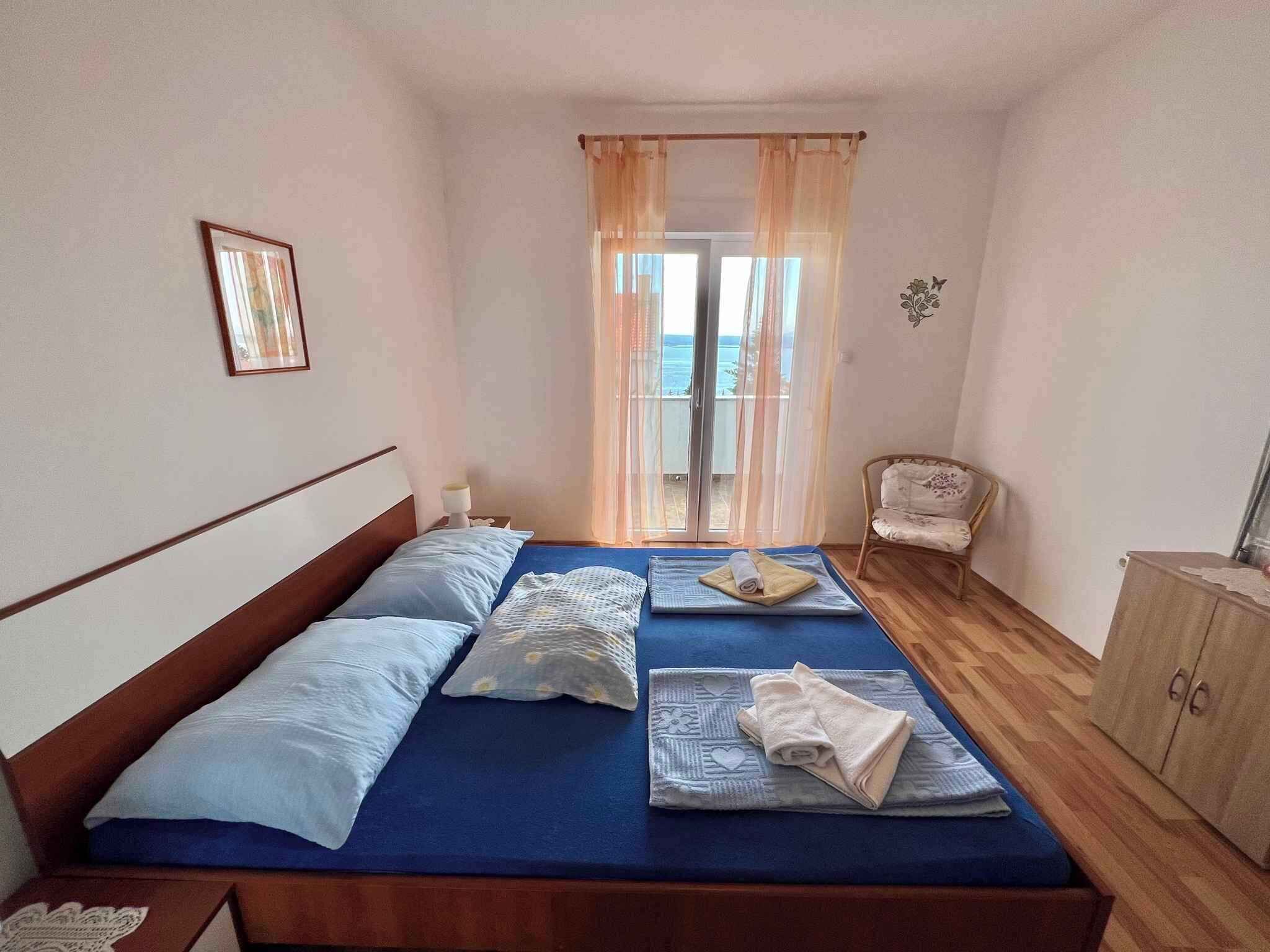 Une chambre à coucher avec un lit, des oreillers, une table de chevet, une chaise et une vue sur la mer par la fenêtre.
