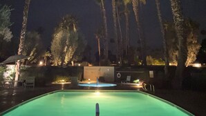 Une piscine éclairée la nuit, entourée de palmiers.