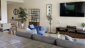 Un salon spacieux avec un grand canapé d’angle, un coin repas comprenant une table et des chaises, un téléviseur fixé au mur et une lampe sur pied.