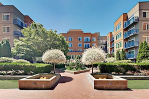 A courtyard with a brick pathway, surrounded by well-maintained hedges and flowering trees.