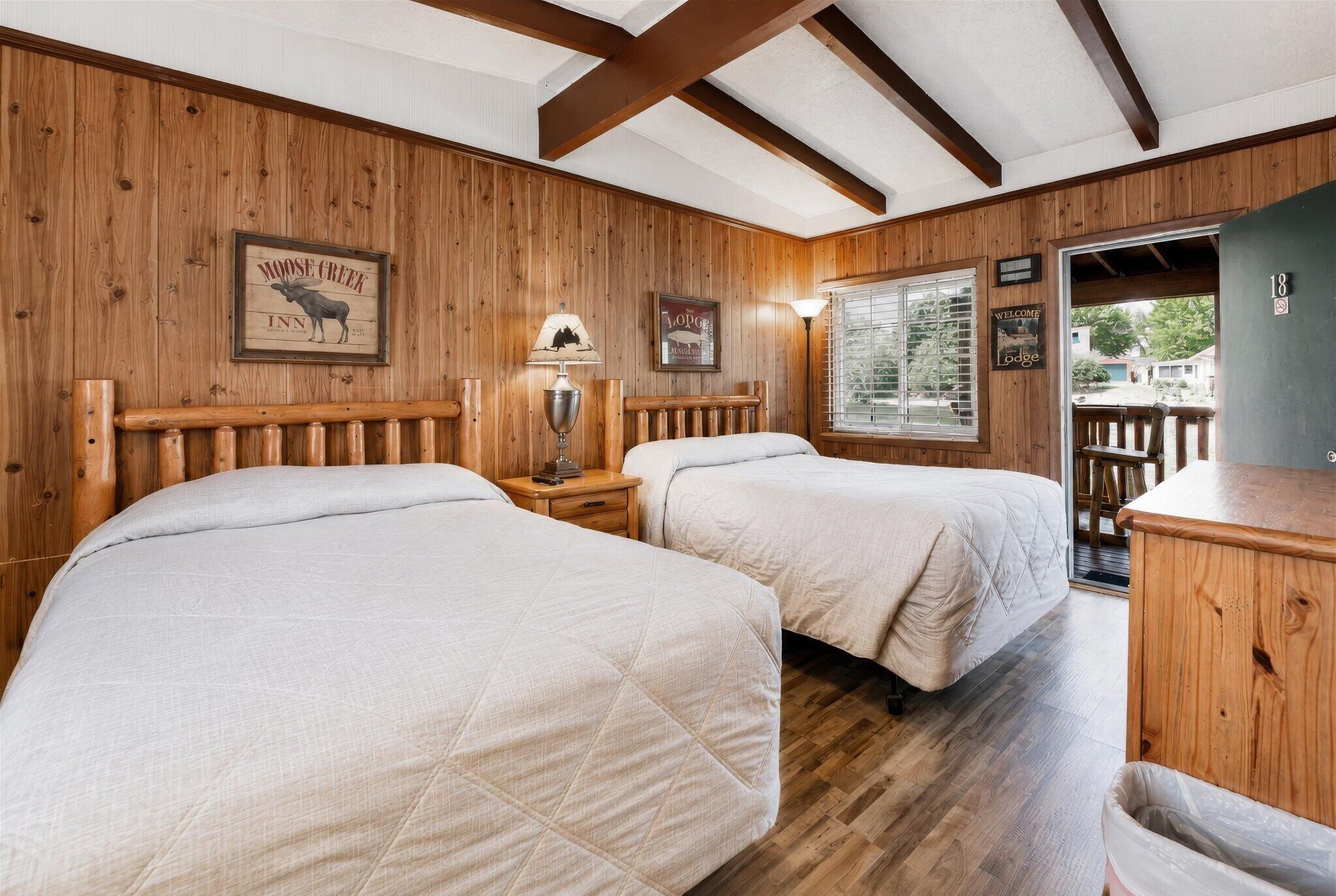 Een kamer met twee bedden, houten wanden, een houten plafond, een raam en een deur naar buiten.