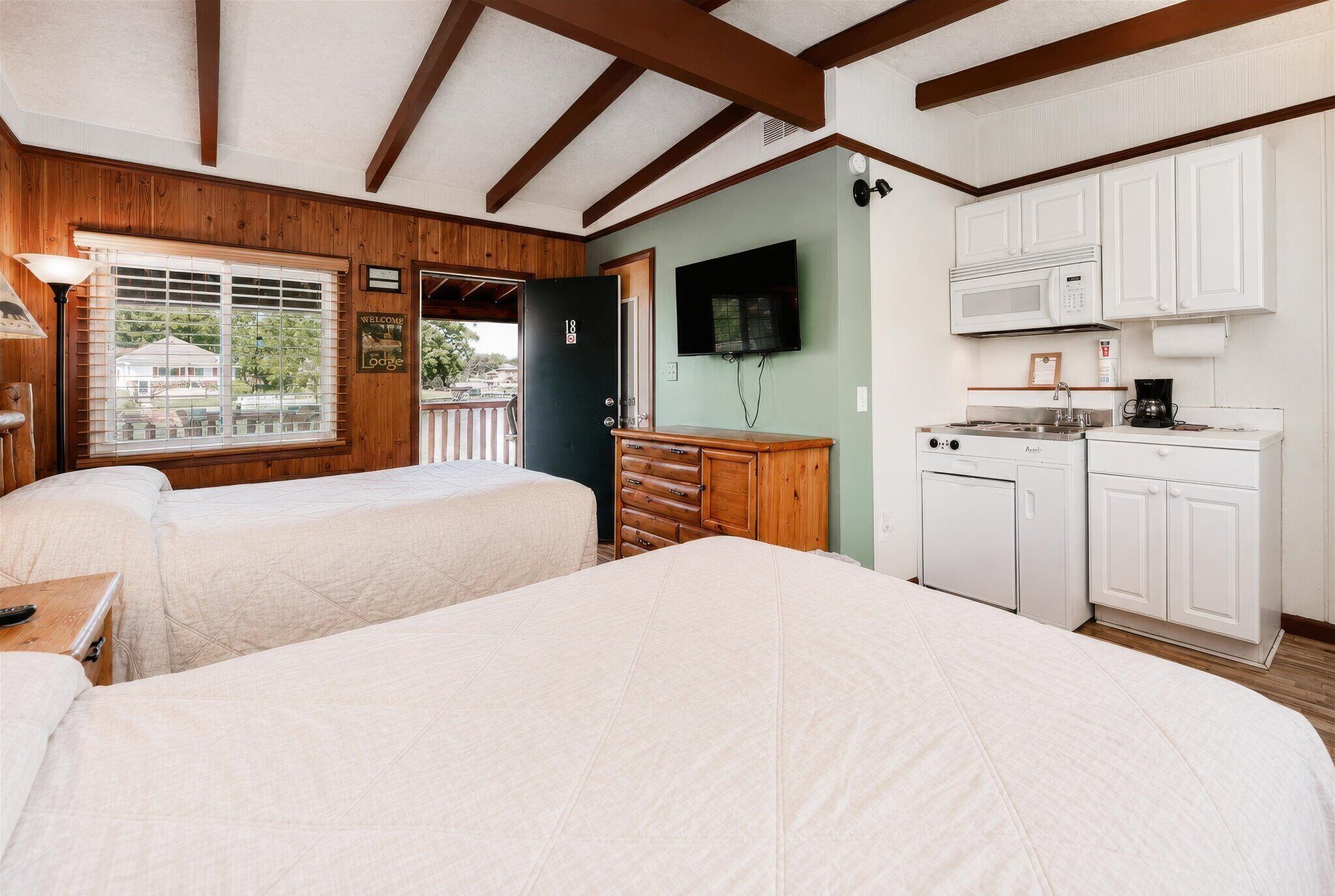 A room with two beds, a wooden dresser, a microwave, a coffee maker, and a television.