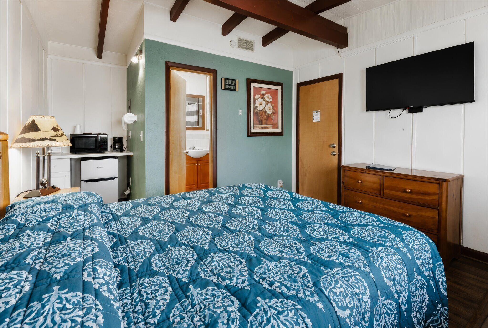 A bedroom with a bed, a dresser, a television, and a kitchenette.
