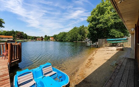 A lakeside dock with a boat and chairs, a sandy beach, and a wooden deck.