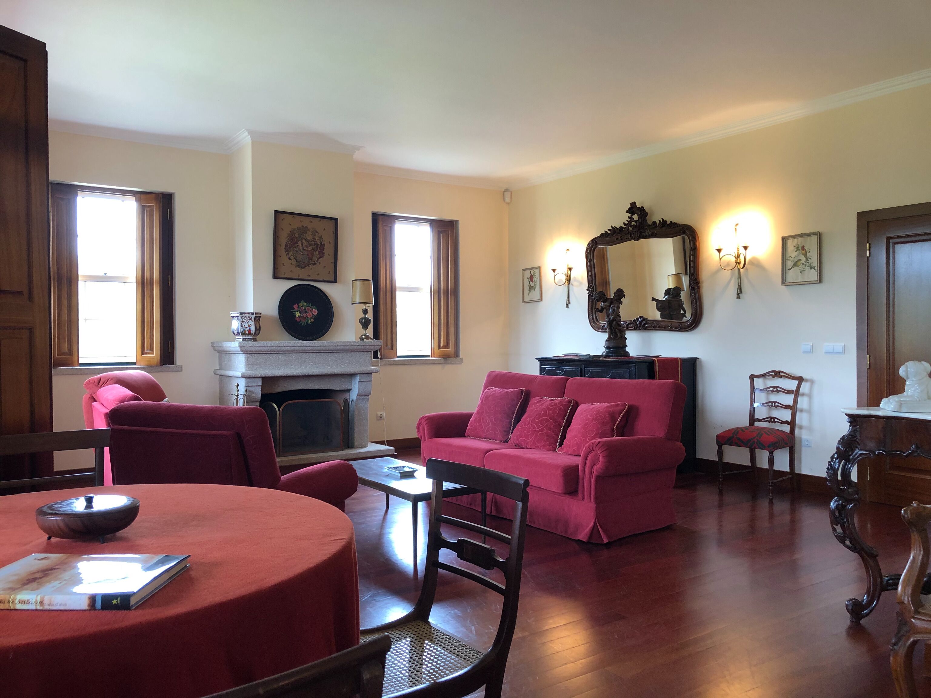 Una sala de estar con chimenea, un sofá rojo, una mesa de comedor con un libro y piso de madera.