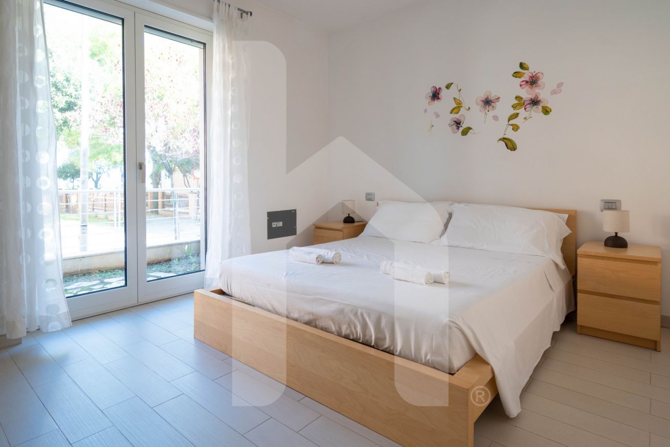 Una camera da letto moderna con un letto in legno, una porta scorrevole in vetro che dà sull'esterno e un piccolo comodino con una lampada.