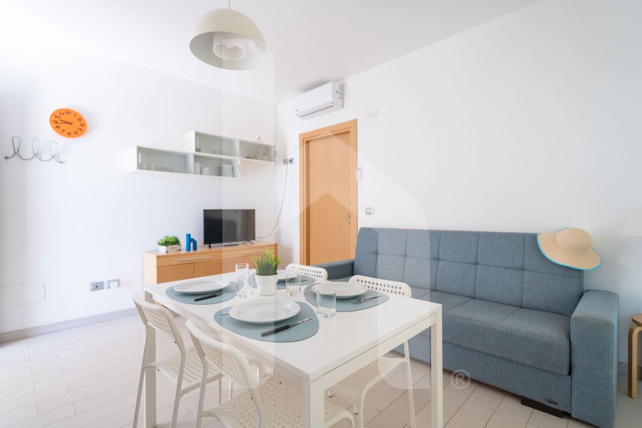Una stanza moderna e luminosa con un tavolo da pranzo apparecchiato per due, un divano blu e un televisore.