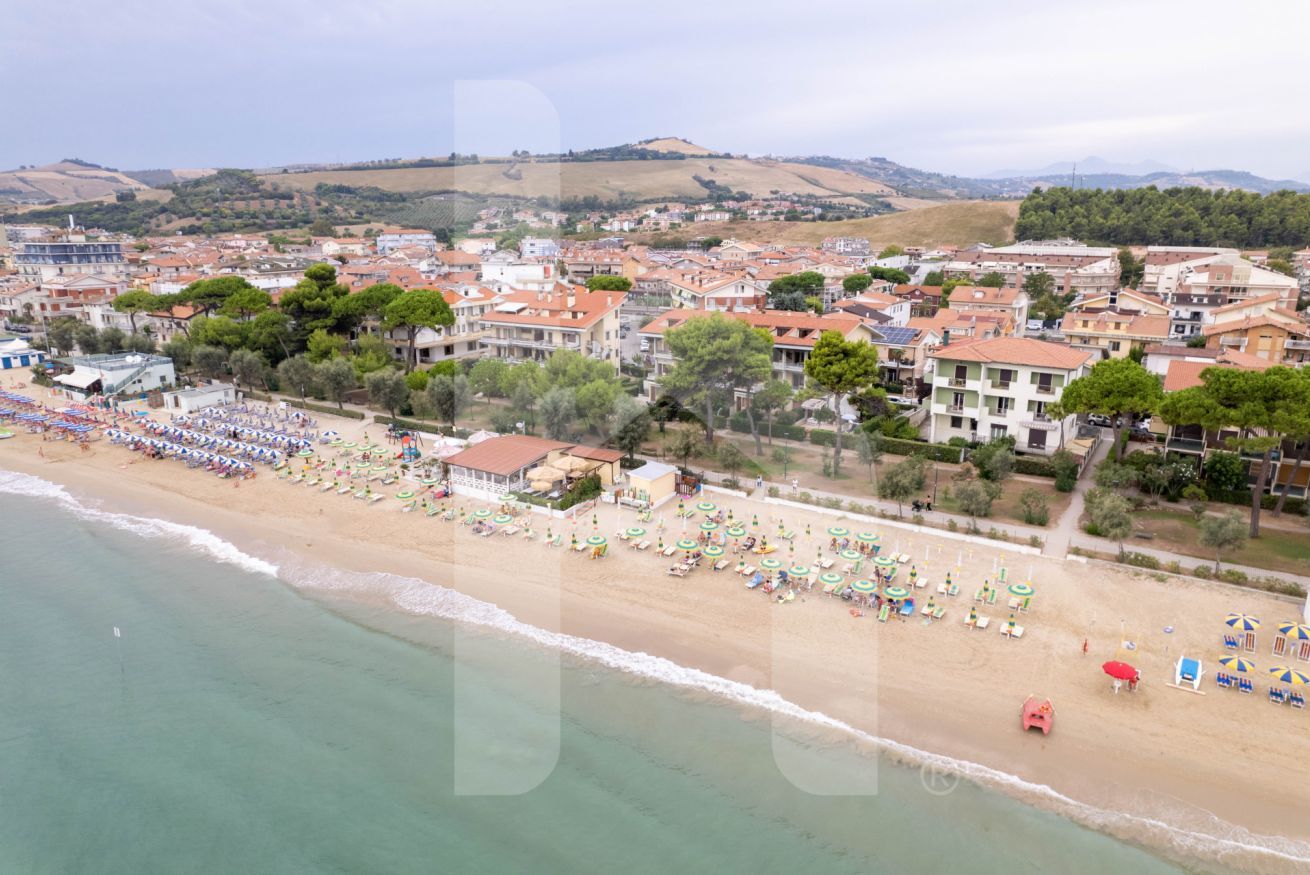 Vue aérienne d’une ville côtière, avec une plage bordée de parasols et de chaises longues.
