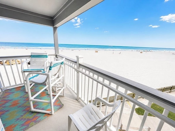 A balcony with a view of the beach, white chairs, and a colorful rug. - Oceanfront condo with pool, patio, central AC, & free WiFi (Myrtle Beach)
