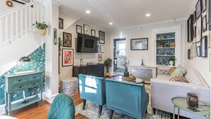 Una sala de estar con una escalera, muebles color turquesa, un televisor y cuadros en las paredes.