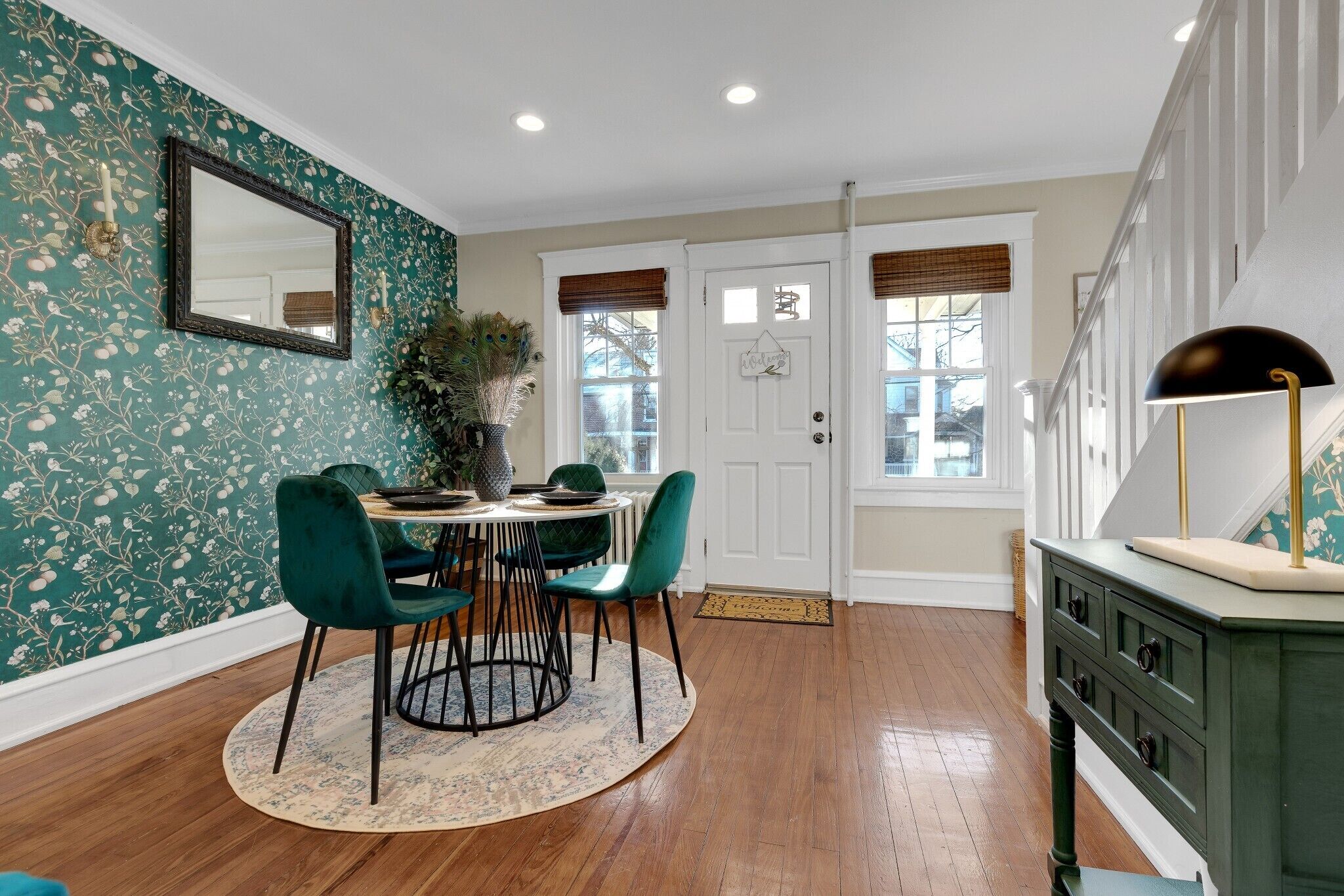A dining area with a round table, green chairs, and a patterned rug.
