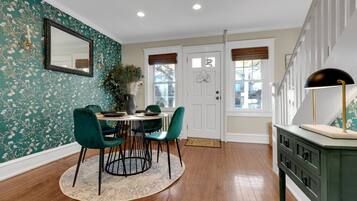 A dining area with a round table, green chairs, and a patterned rug.