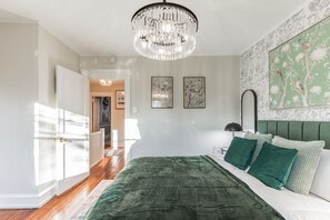 A bedroom with a green upholstered bed, a chandelier, and a floral wallpaper design. - Homey Retreat in Historic Kennett Square!! (Kennett Square)