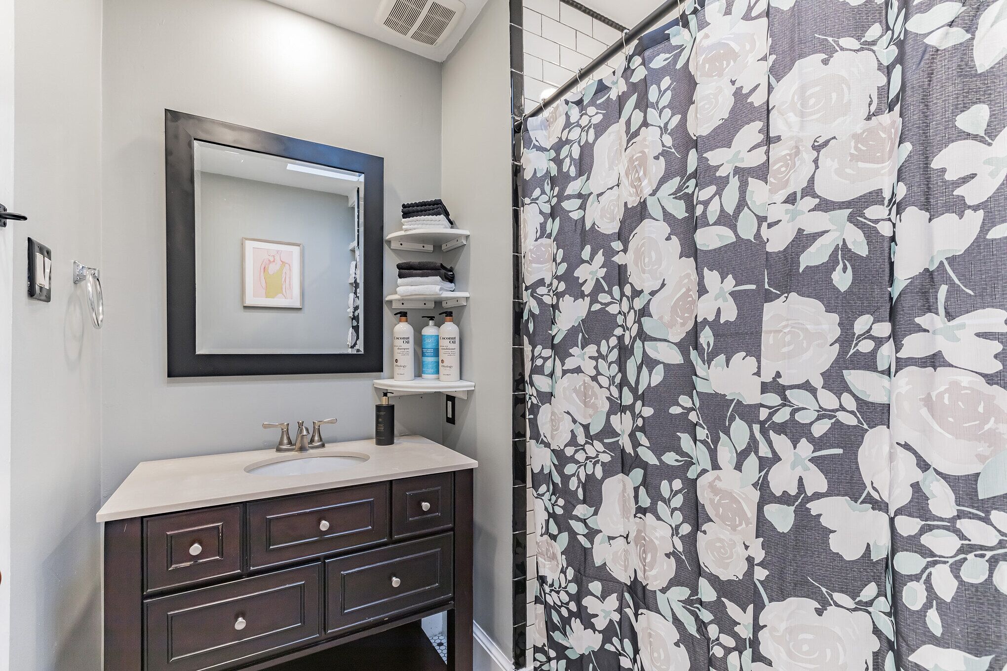 Une salle de bain avec un meuble-lavabo foncé, un miroir et un rideau de douche à motifs floraux.